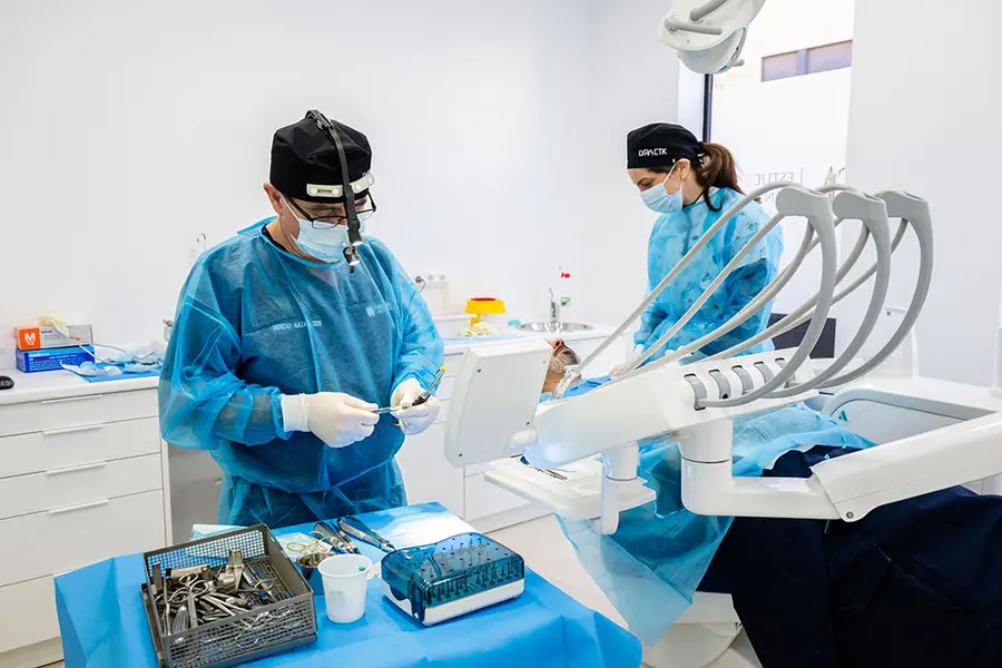 A surgeon with loupes working at the chair beside the laid-out instruments