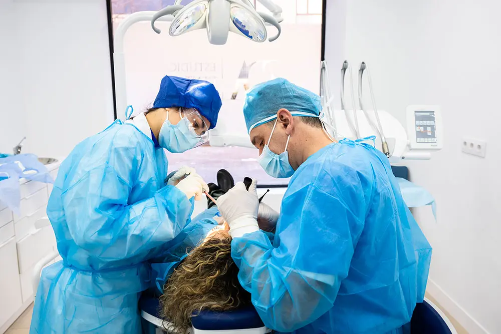 Three clinicians in surgical gowns working around a patient under the operating light