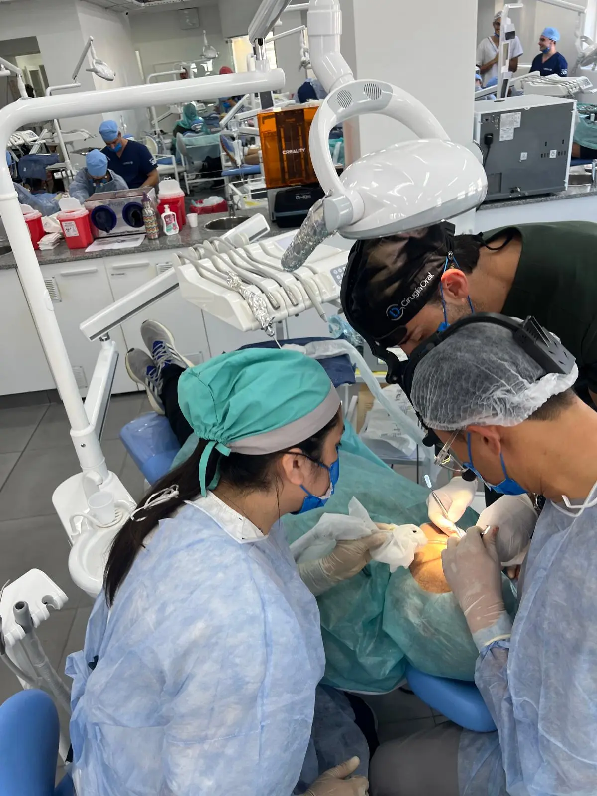 Four participants operating together on a patient, seen from the foot of the chair